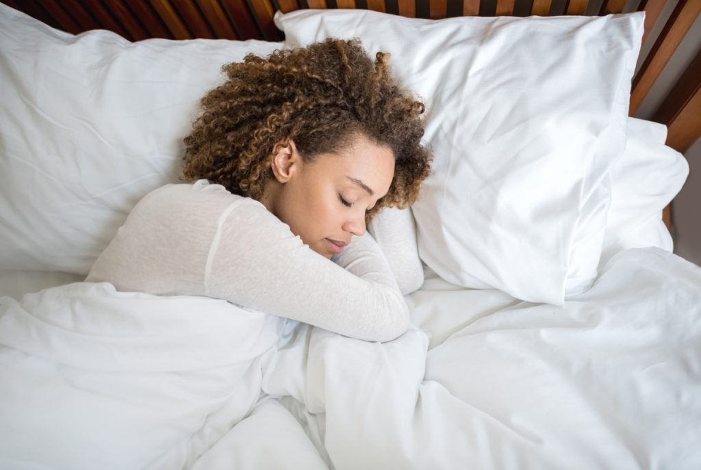 woman with curly brown hair sleeping on side in bed with white linens